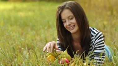 Genç güzel kadın yeşil çimenlerin üzerinde yatıyor ve olgun üzüm yemek.
