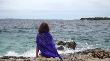 Ağır çekim: küçük güzel kız kayalar denize kıyı yakınındaki oturur ve mesafe içine görünüyor.