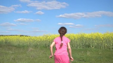Ağır çekim: Güzel küçük kız mutlu yaz alan arka planı sarı çiçek açan törpülemek ile çalışıyor.