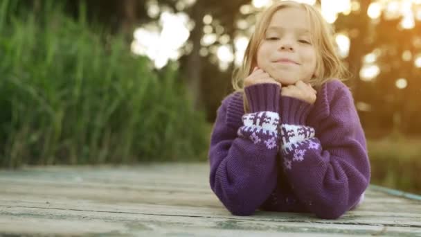 Little beautiful girl lies on the river pier and smiling. — Stock Video