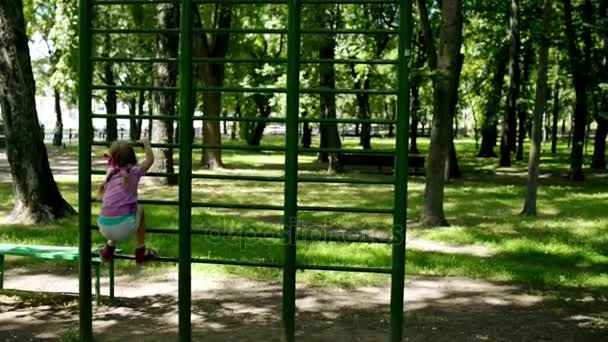 Pequeña chica hermosa se dedica a los deportes en barras horizontales en el parque de la ciudad de verano . — Vídeos de Stock