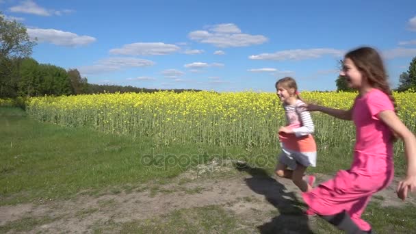 Movimiento lento: Dos hermosas hermanas pequeñas corren felizmente contra el fondo del campo de verano con escofina de floración amarilla . — Vídeo de stock