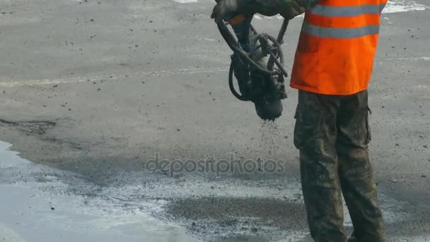 特別な装置の助けを借りて、アスファルトや砂利道路上の穴を修復する建設労働者. — ストック動画