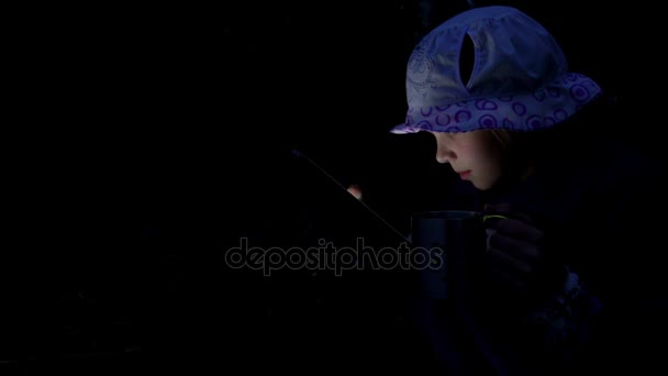 Small beautiful girl reads on tablet computer at dusk against backdrop of an autumn forest lake. — Stock Video