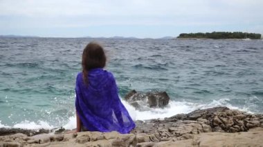 Ağır çekim: küçük güzel kız kayalar denize kıyı yakınındaki oturur ve mesafe içine görünüyor.