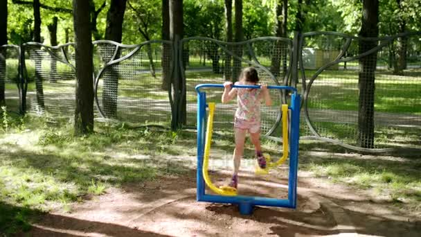 Petite belle fille engagée sur des appareils de formation sportive dans le parc de la ville d'été . — Video