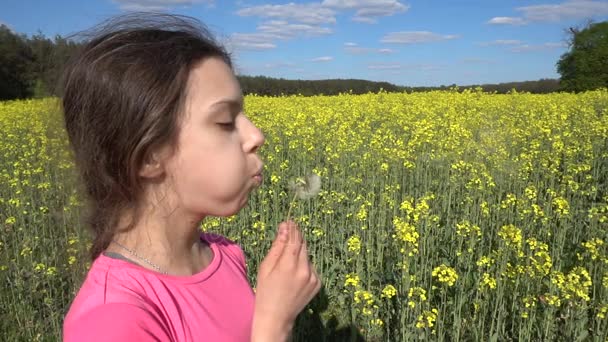 Malá krásná dívka foukání na bílém Pampeliška proti žluté letní řepkové pole.