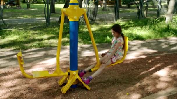 Маленькая красивая девочка занимается на спортивном тренажере в летнем городском парке . — стоковое видео