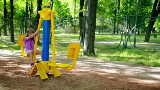 Niña hermosa dedicada a aparatos de entrenamiento deportivo en el parque de la ciudad de verano . — Vídeos de Stock