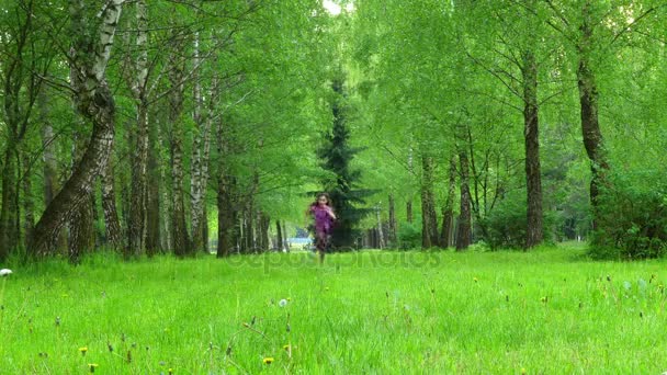 Niña hermosa caminando a través de hierba verde en el parque de la ciudad de verano . — Vídeos de Stock