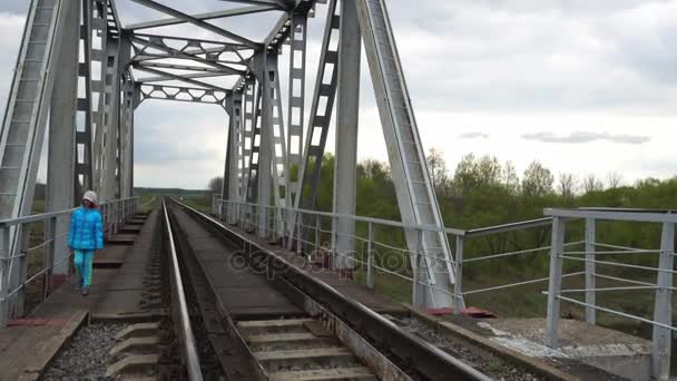 Piccola bella ragazza sta camminando lungo il ponte ferroviario in campagna . — Video Stock