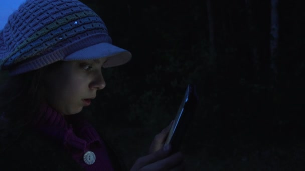 小さな美しい少女を背景に秋の森林湖の夕暮れ時にタブレット コンピューターの読み取り. — ストック動画
