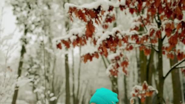 暖かいジャケットで美しい少女雪に覆われた冬の公園でベンチに座っているし、携帯電話上で再生. — ストック動画