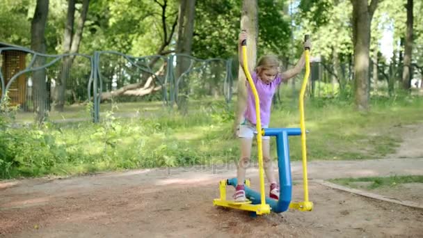 Lilla vackra flicka förlovad på sport utbildning apparater i sommar stadspark. — Stockvideo