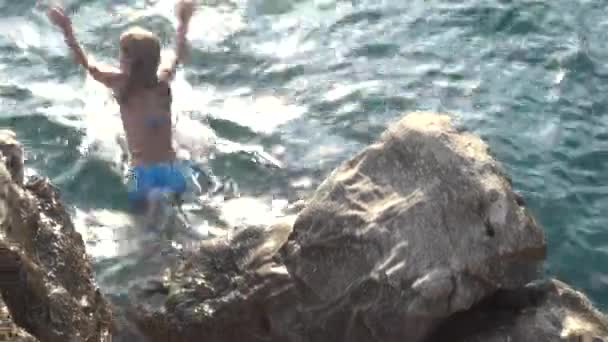 Niña hermosa saltando de piedra a mar en la costa adriática de Croacia . — Vídeo de stock