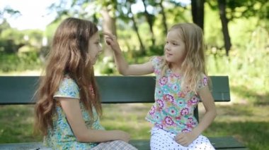 İki küçük güzel kız kardeş yaz şehir Park ahşap Bank oynamak.