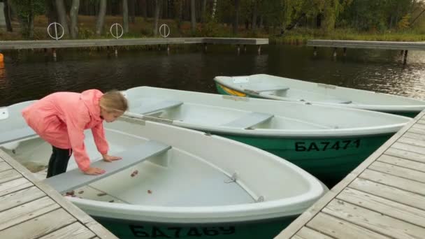 Piccola bella ragazza in impermeabile rosa su piccola barca al molo del fiume . — Video Stock