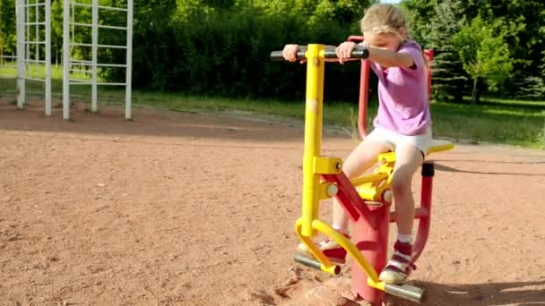 Lilla vackra flicka förlovad på sport utbildning apparater i sommar stadspark. — Stockvideo