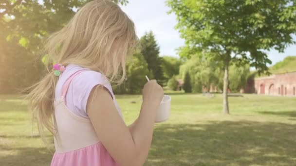 Маленькая красивая девочка ест вкусное мороженое в летнем зеленом парке . — стоковое видео
