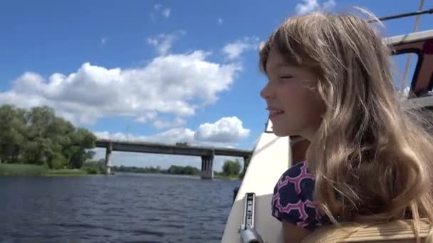 Belle petite fille souriante aux cheveux longs nage sur le bateau sur la rivière sous un grand pont en béton . — Video