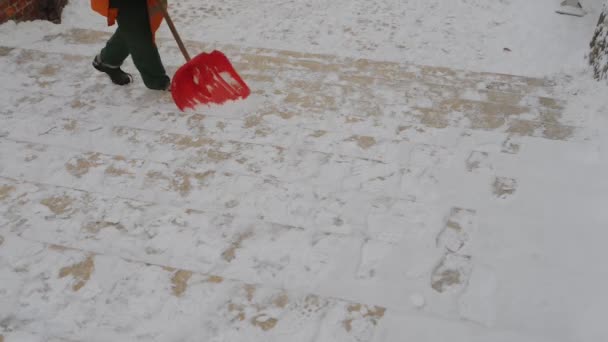 Travailleur de rue en salopette orange nettoie la neige avec une pelle à partir des marches des escaliers . — Video