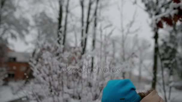 Niña hermosa en chaqueta caliente se sienta en el banco en el parque nevado de invierno y juega en el teléfono móvil . — Vídeo de stock