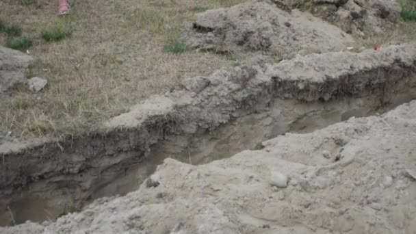 Bambina salta sopra un fosso di terra, scavato per la posa di tubi . — Video Stock