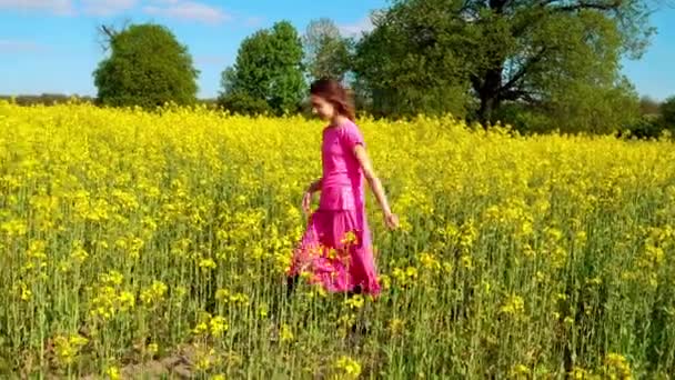 Piccola bella ragazza sta camminando lungo il campo di colza giallo . — Video Stock