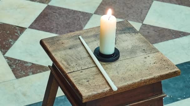 Burning candle on backless stool against background of marble floor. — Stock Video