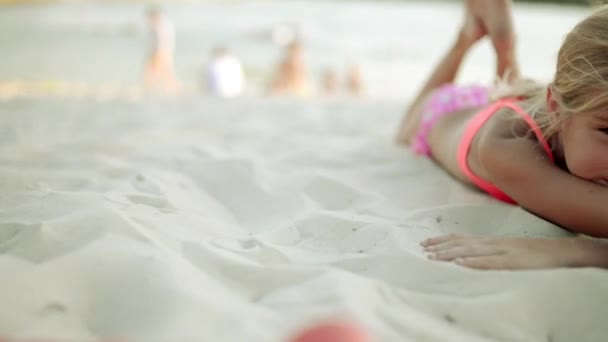 Small beautiful girl lies on white sand of large lake beach. — Stock Video