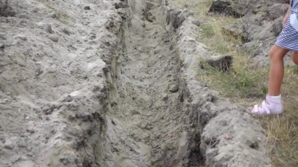 Little girl jumps over an earthen ditch, dug for laying pipes. — Stock Footage Little girl jumps over an earthen ditch, dug for laying pipes. Stock Footage