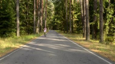 Güzel genç kız yaz orman yollarında asfalt boyunca bisiklet sürme.