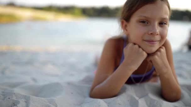 Kleine mooi meisje ligt op het witte zand van groot meer strand. — Stockvideo