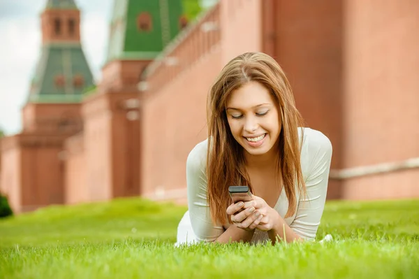 Mladá krásná žena smějící se leží na zeleném trávníku s mobilním telefonem — Stock fotografie