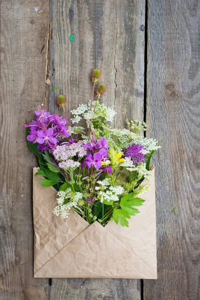 Wild field flowers in craft paper envelope over wooden backgroun — Stock Photo, Image