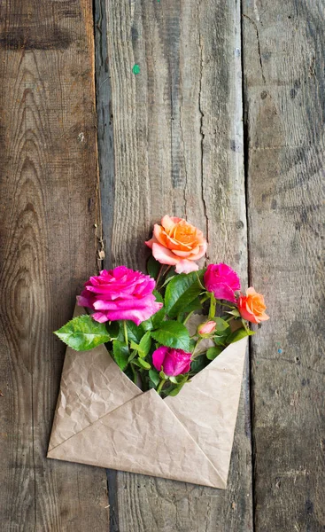 Квіти троянд в ремісничому папері конверт на дерев'яному фоні — стокове фото