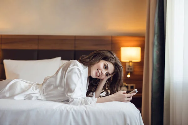 Mosolygó lány az ágyon a telefon — Stock Fotó