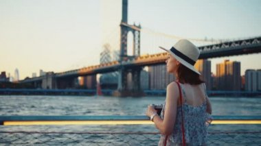Güneş batarken Manhattan Köprüsü 'nde retro kameralı çekici bir kız.