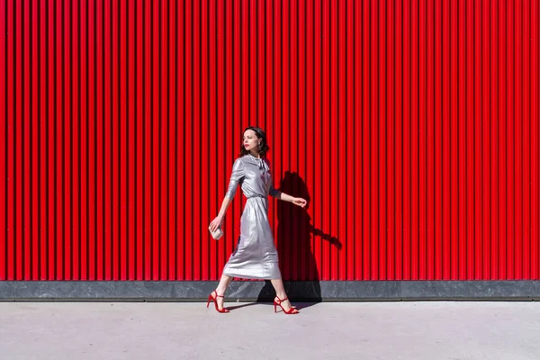 Menina atraente nos saltos na parede vermelha — Fotografia de Stock