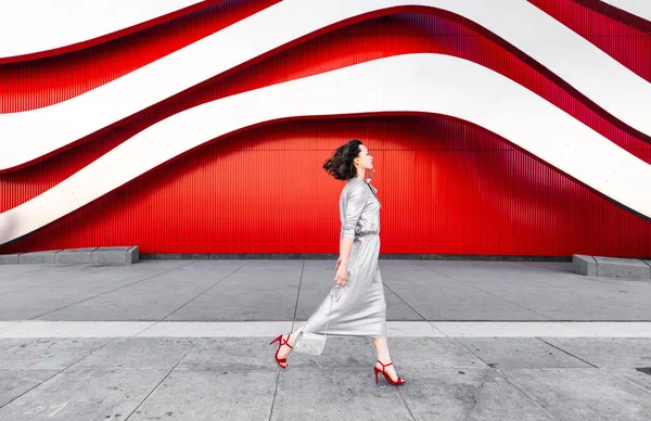 Mladá žena v podpatcích u červené zdi — Stock fotografie