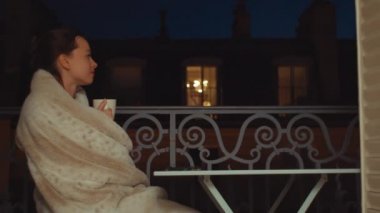 Young woman drinking tea on the balcony at night