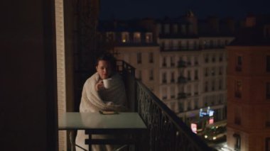 Young girl drinking tea on a balcony in Paris at night