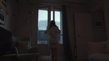 Young woman in a white shirt opening the door to the balcony