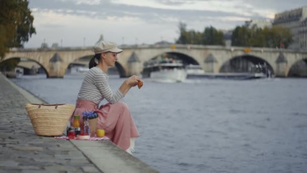 パリで川のそばでクロワッサンを食べる若い女の子 — ストック動画
