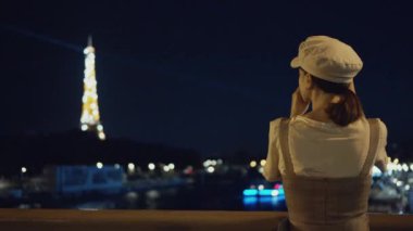 Gece Eyfel Kulesi 'nin fotoğrafını çeken genç bir turist.