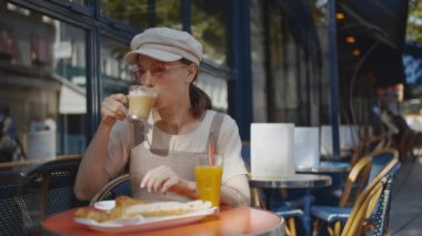 Gülümseyen kız Paris 'teki açık kafede kahvaltı yapıyor.
