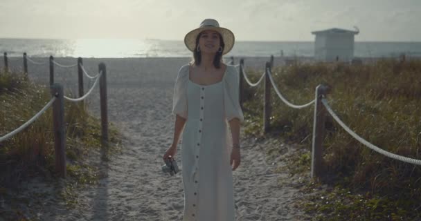 Chica joven con una cámara retro en la playa — Vídeo de stock