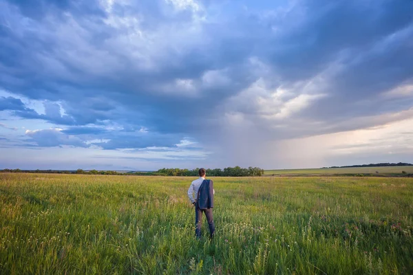 Empresário em um terno andando em um campo verde espaçoso com um céu azul — Fotografia de Stock