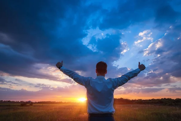 Glad affärsman, stående i fältet över vind bakgrund med hans händer upp och tummen upp — Stockfoto