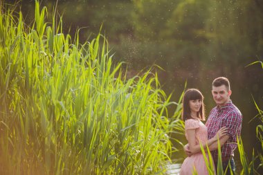Göldeki aşıklar. Bu genç adam gün batımında gitar çalarken genç çift parkta, suyun kenarında oturuyor..